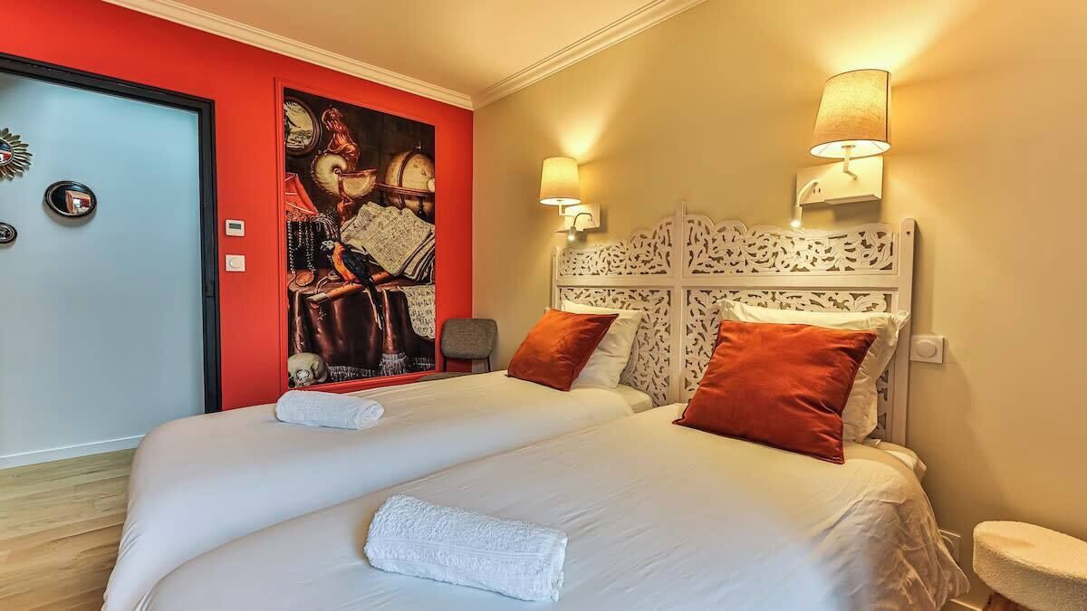 A double bed with white linens, two red pillows, and a white throw blanket. There are two wall-mounted lamps on either side of the bed.