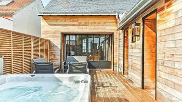 A wooden exterior wall, a hot tub, and a patio area with chairs and a table.