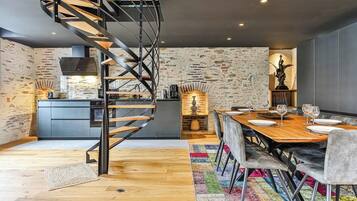 Une cuisine moderne avec un escalier en colimaçon, un coin repas avec une table et des chaises en bois, et un mur en pierre.