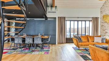 A modern living room with a sofa, a dining area with a table and chairs, and a spiral staircase.