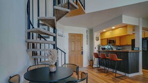 A modern kitchen with wooden cabinets, a black refrigerator, and a bar area with orange stools. - Warm & Cozy Condo • Prime Angel Fire Location (Angel Fire)