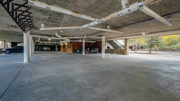 An underground parking garage with concrete pillars, exposed pipes, and a staircase leading to upper levels.