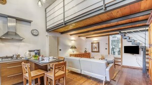 Una cocina moderna con armarios de madera, un comedor con mesa y sillas, un sofá y una escalera que sube a otro nivel.