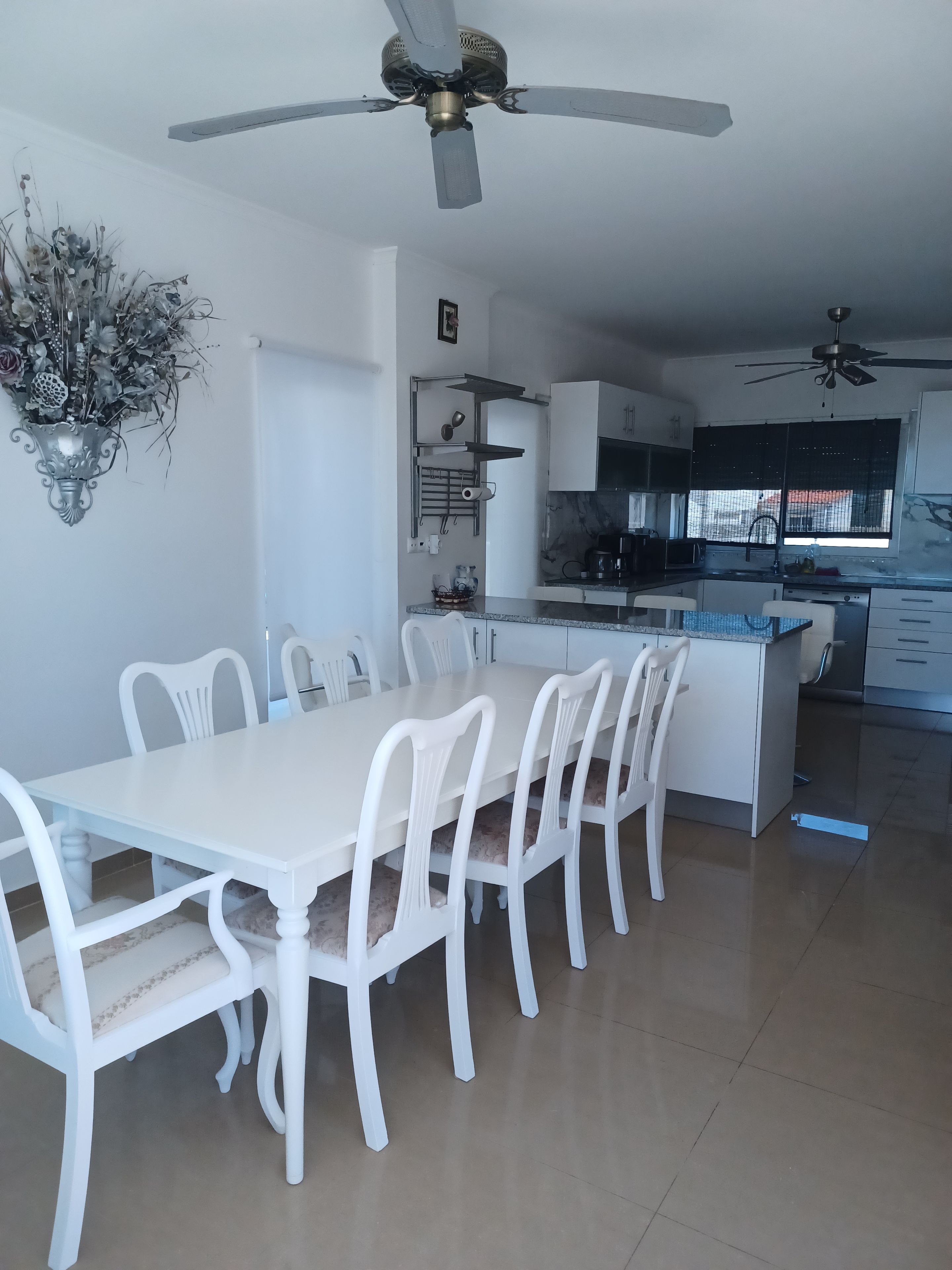 A modern kitchen with white cabinetry, a dining area with white chairs, and ceiling fans.
