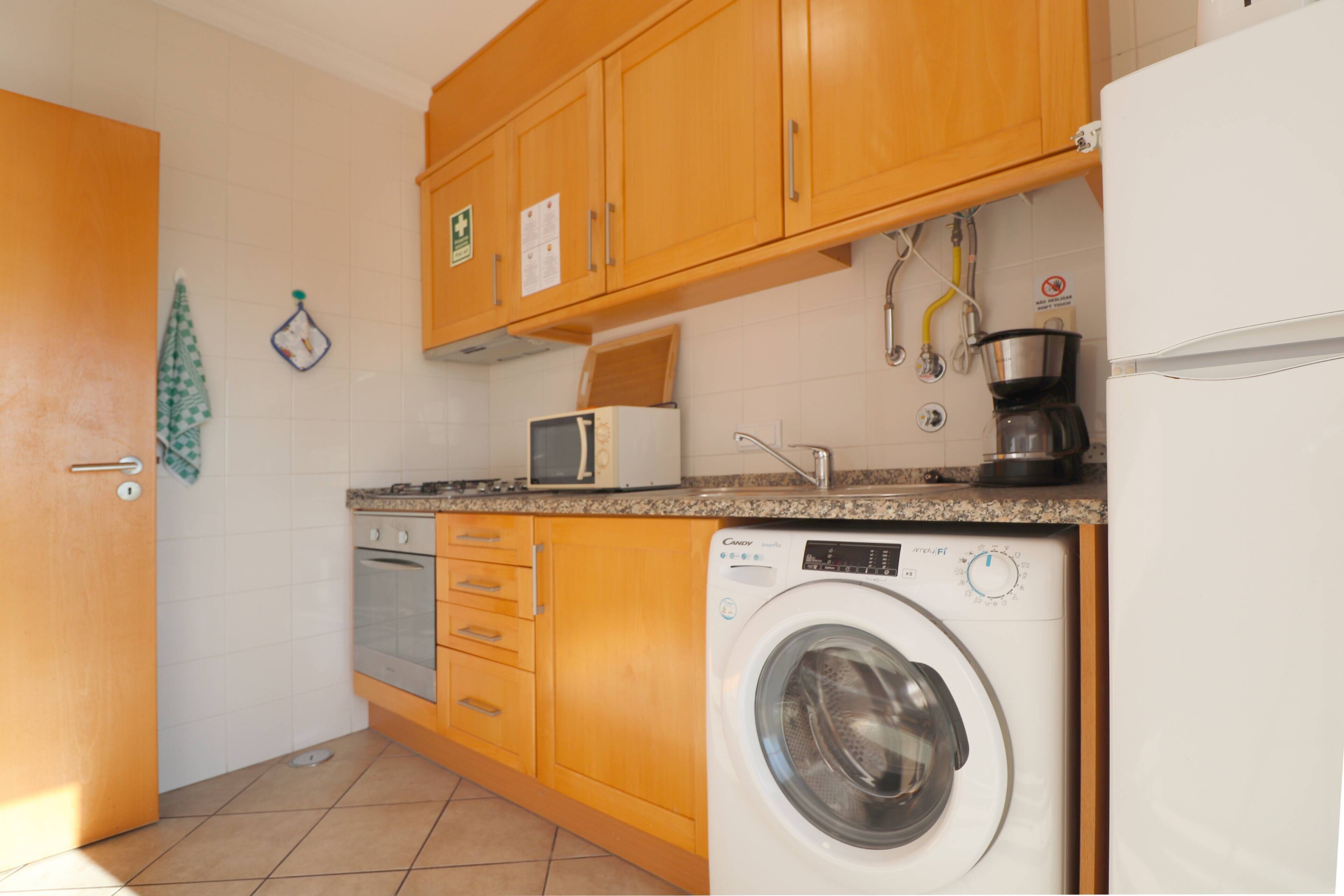 Cocina compacta con armarios de madera, microondas, lavadora y cafetera.