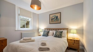 Une chambre à coucher avec un grand lit, des lampes de chevet, une fenêtre et une œuvre d’art encadrée au mur.