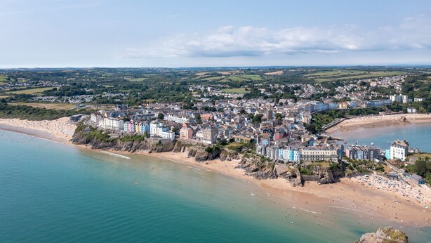 Une vue aérienne d’une ville côtière, avec des bâtiments le long de la plage, un ciel dégagé et une mer calme.