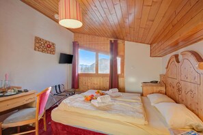 A room with a wooden ceiling, a bed with white linens, a desk with a chair, a television on the wall, and a window with curtains. - Hotel Relais Alpin Single Ski In-Out 2 125, Les Mosses, Switzerland (Les Mosses)