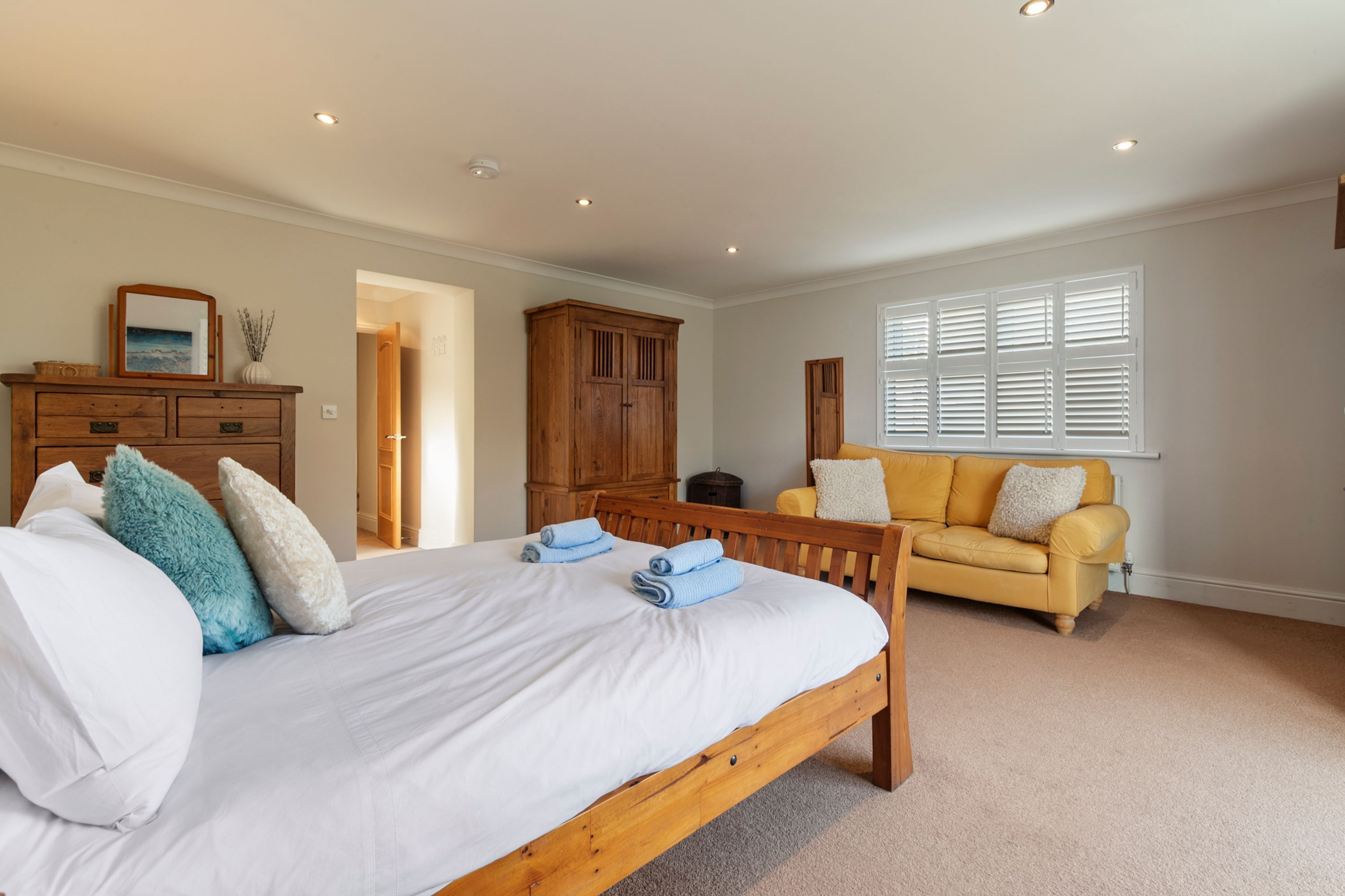 A bedroom with a wooden bed, a yellow sofa, and a large window with blinds.