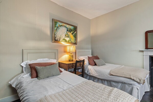 A hotel room with two single beds, a desk with a lamp, a painting on the wall, and a fireplace. - 2 Olive Buildings - Within the Town Walls (Tenby)