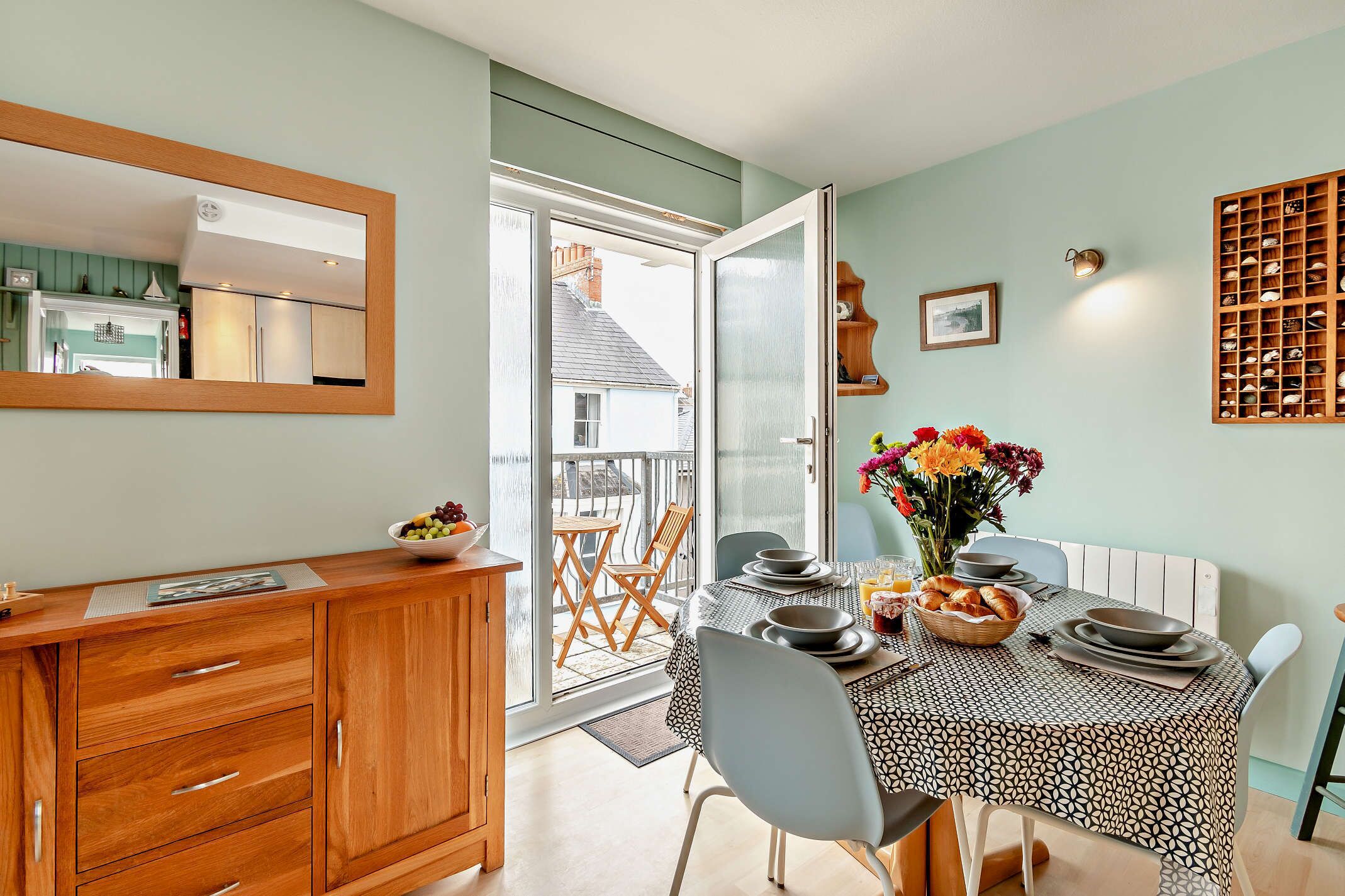 A dining area with a table set for four, a wooden cabinet, and a view of the outside balcony.