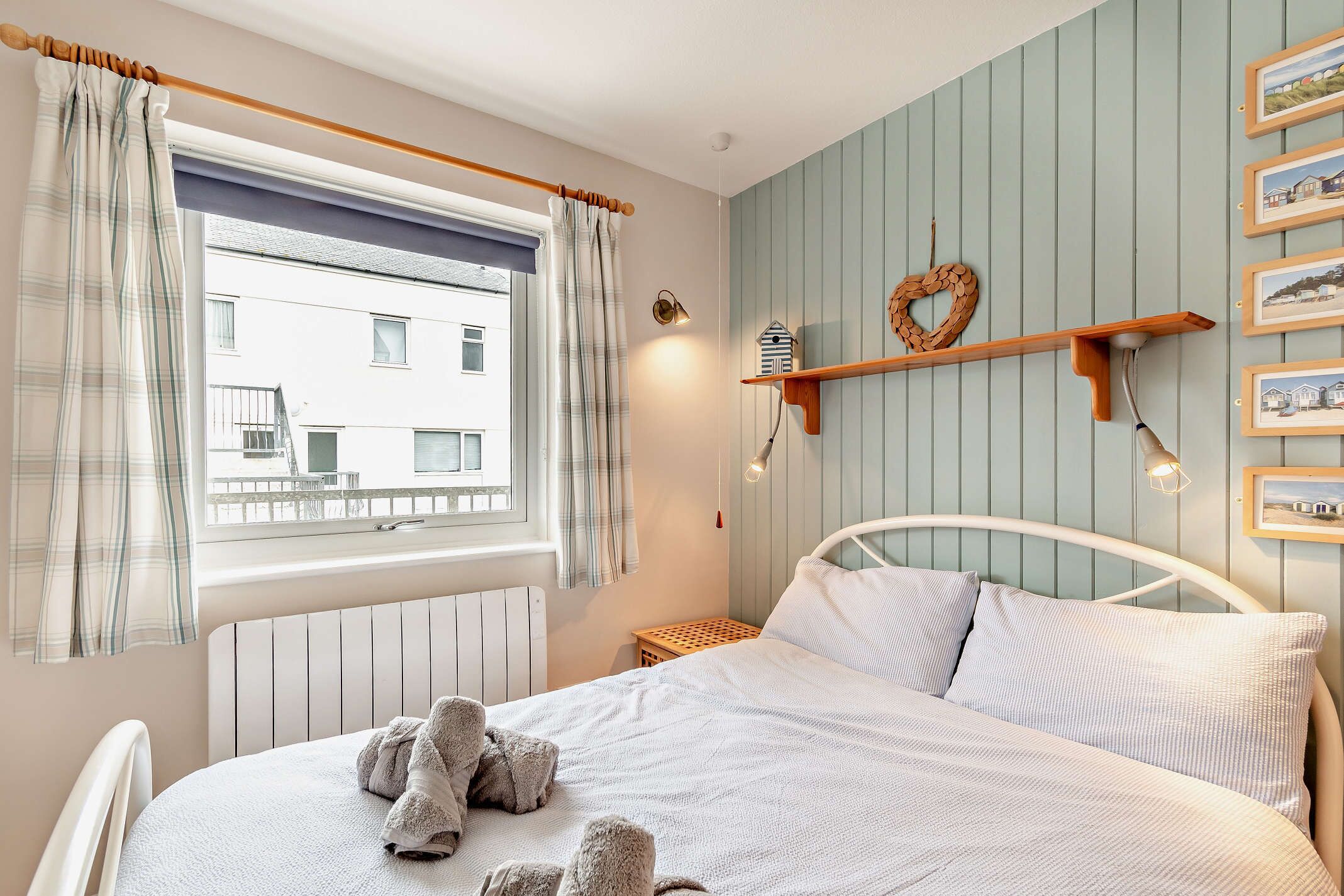 Ett sovrum med en säng, ett fönster med gardiner, en vägghylla med bilder och ett element.