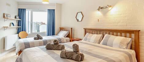 A hotel room with two beds, a window with curtains, a wall-mounted mirror, and a bedside table.