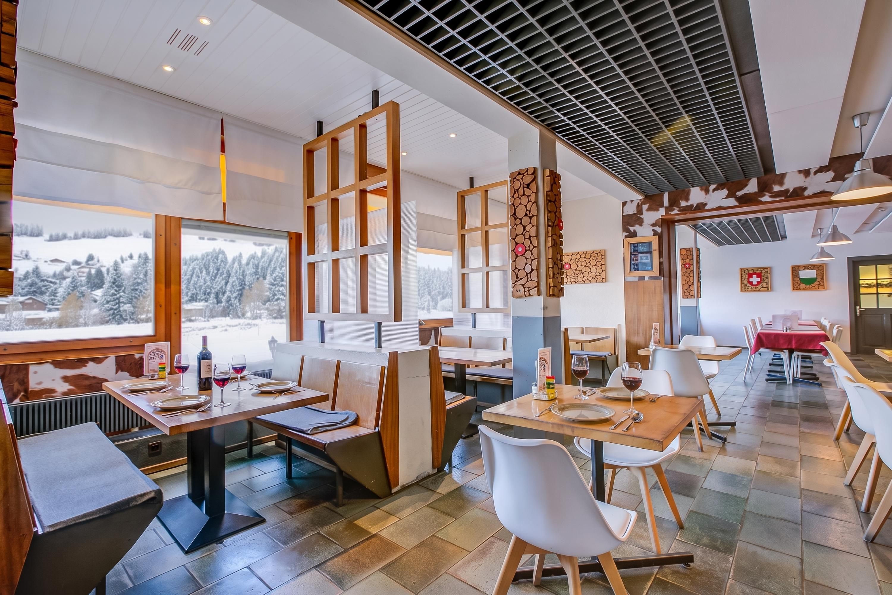 A restaurant with a view of snow-covered trees, wooden furniture, and a modern ceiling design.