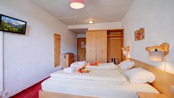 Ein Hotelzimmer mit einem Bett, einem Holzschrank, einem Schreibtisch, einem Telefon und einem an der Wand befestigten Fernseher.
