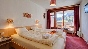 Une chambre d’hôtel avec deux lits, une table avec des chaises, une vue sur les montagnes et un téléviseur fixé au mur.