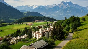 Un village de montagne aux bâtiments traditionnels, doté d’une route pavée et offrant une vue sur des sommets enneigés en arrière-plan.