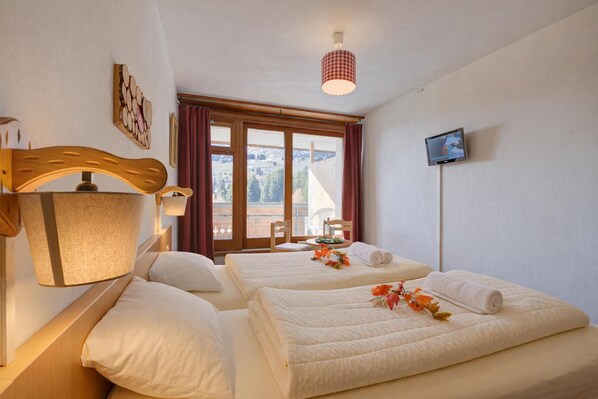 Ein Hotelzimmer mit zwei Betten, einem Fernseher, einem Fenster mit Vorhängen und einer Lampe.