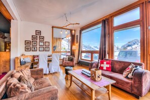 A cozy living room with a fireplace, wooden furniture, and large windows offering a mountain view.