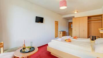 Ein Hotelzimmer mit einem Bett, einem kleinen Tisch mit Flasche und Gläsern, einem an der Wand montierten Fernseher und einem Holzschrank.