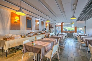 Een restaurant met meerdere tafels, verlichting aan het plafond en uitzicht op het omliggende landschap.