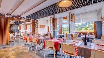 Ein Restaurant mit mehreren gedeckten Tischen, großen Fenstern mit Blick auf die Landschaft und einem modernen Interieur.