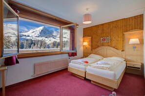 Une chambre d’hôtel avec un lit, une fenêtre donnant sur des montagnes enneigées, une tête de lit en bois et un radiateur.