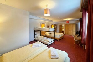 Une chambre d’hôtel avec des lits superposés, un bureau, une chaise, une lampe et une armoire.