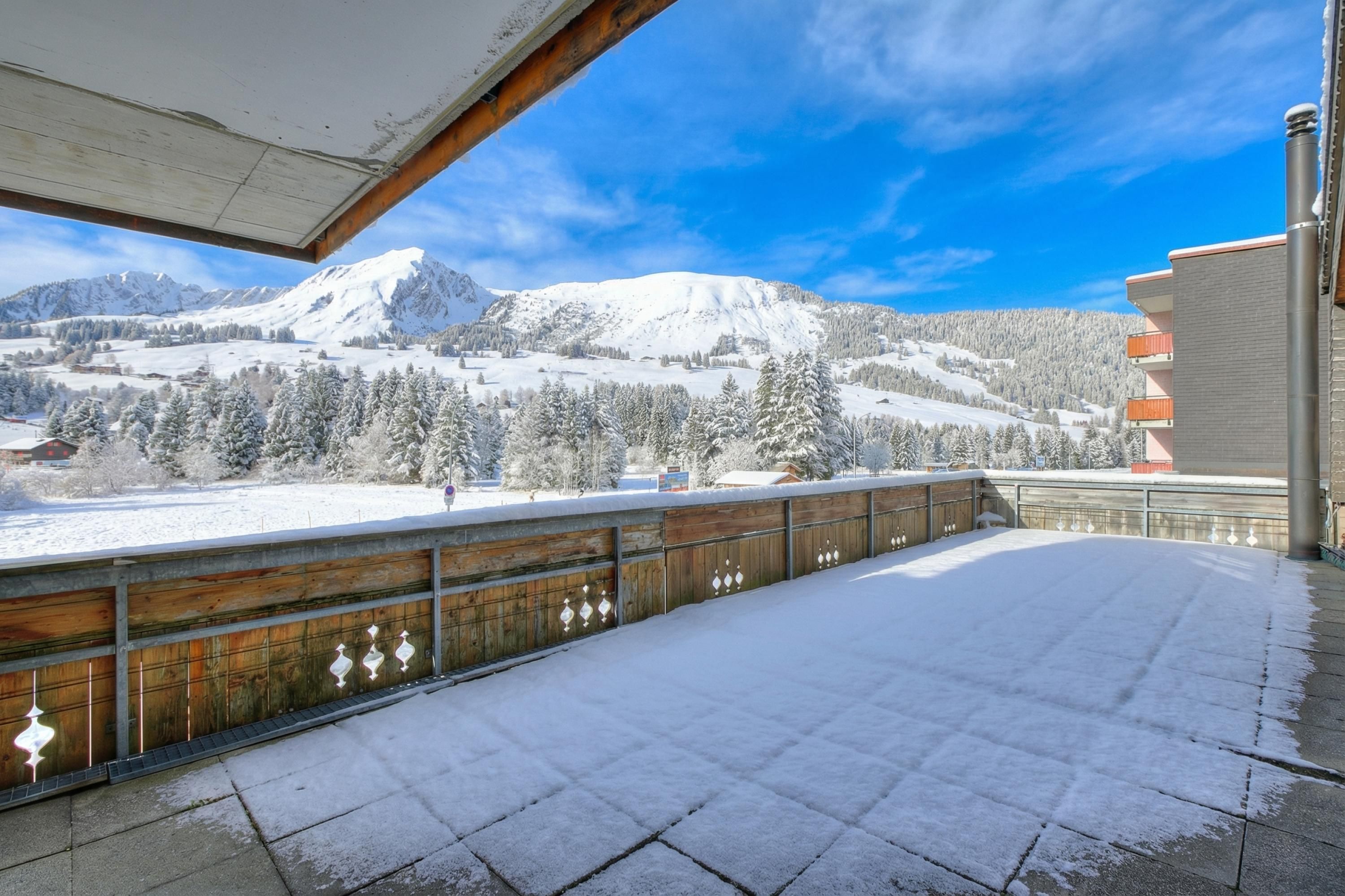 Un balcón cubierto de nieve con vistas a una cordillera y un edificio con balcones.