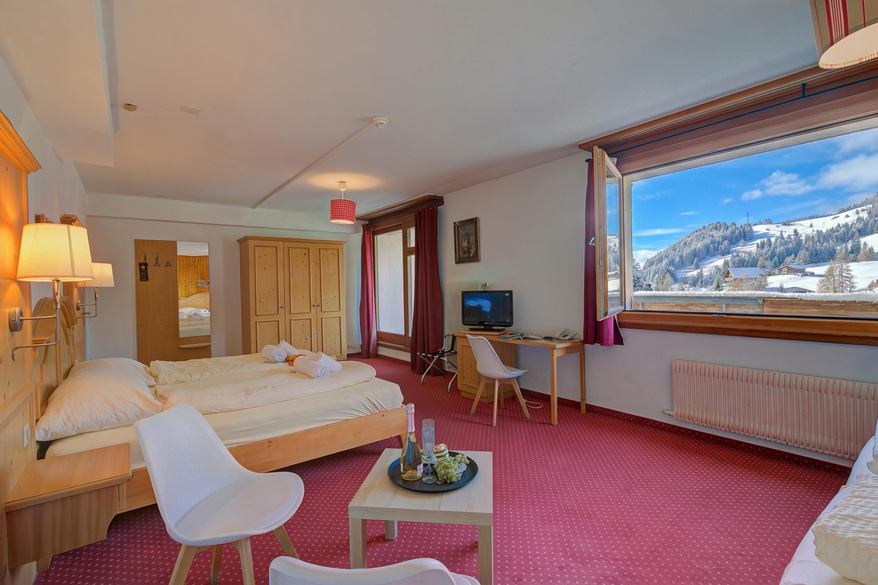 A hotel room with a bed, a desk, a chair, a television, and a window with a mountain view.