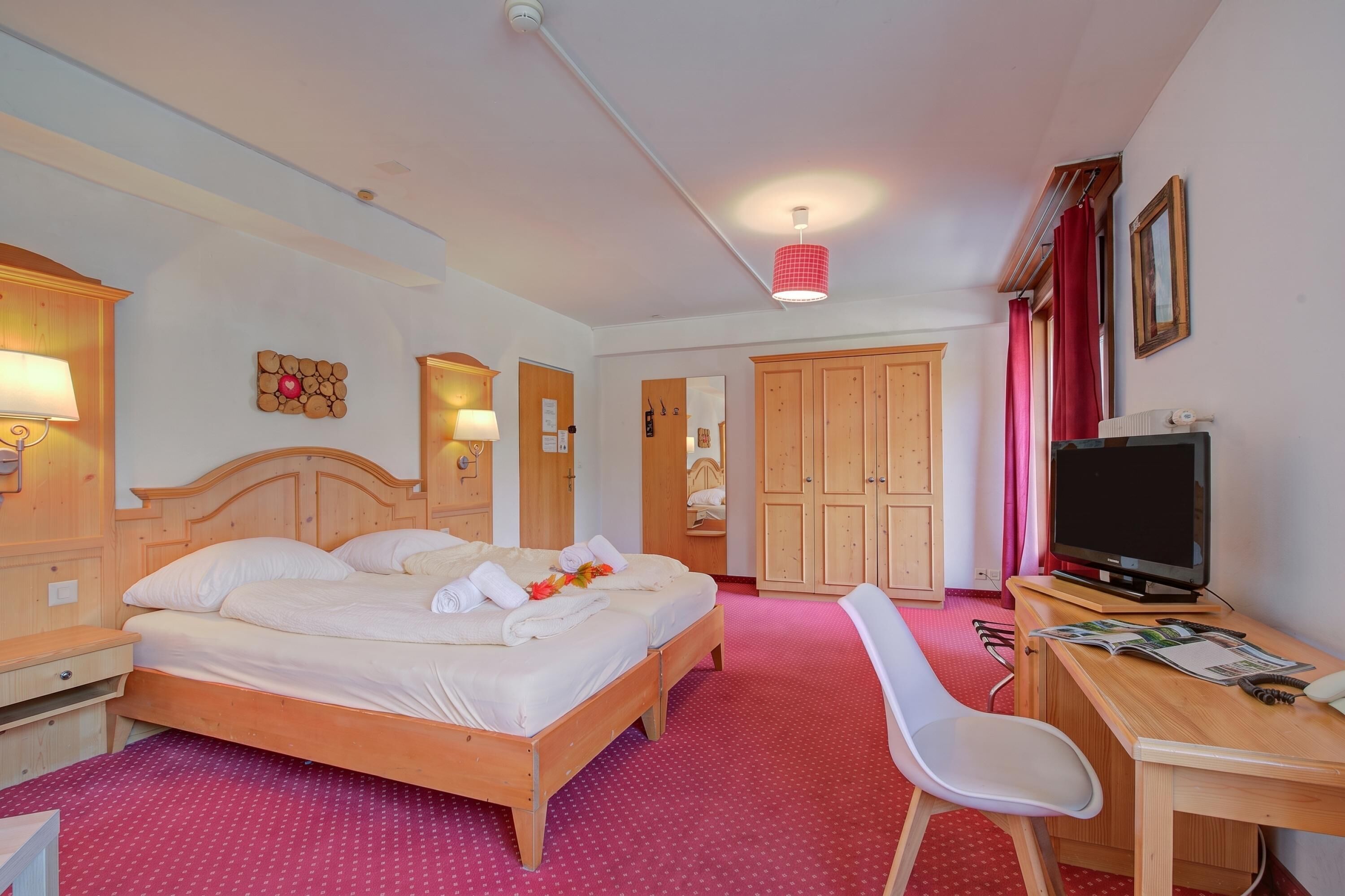 Una habitación de hotel con una cama de madera, un escritorio con un ordenador, un televisor y una silla.