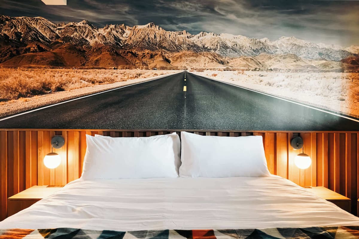 Una cama con sábanas blancas y dos almohadas, con cabeceros de madera que incluyen luces fijadas a la pared.