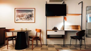 A compact hotel room with a checkered floor, a round table with two chairs, a bed, a TV mounted on the wall, and a framed picture above the table. - La Vista Motel (Denver)