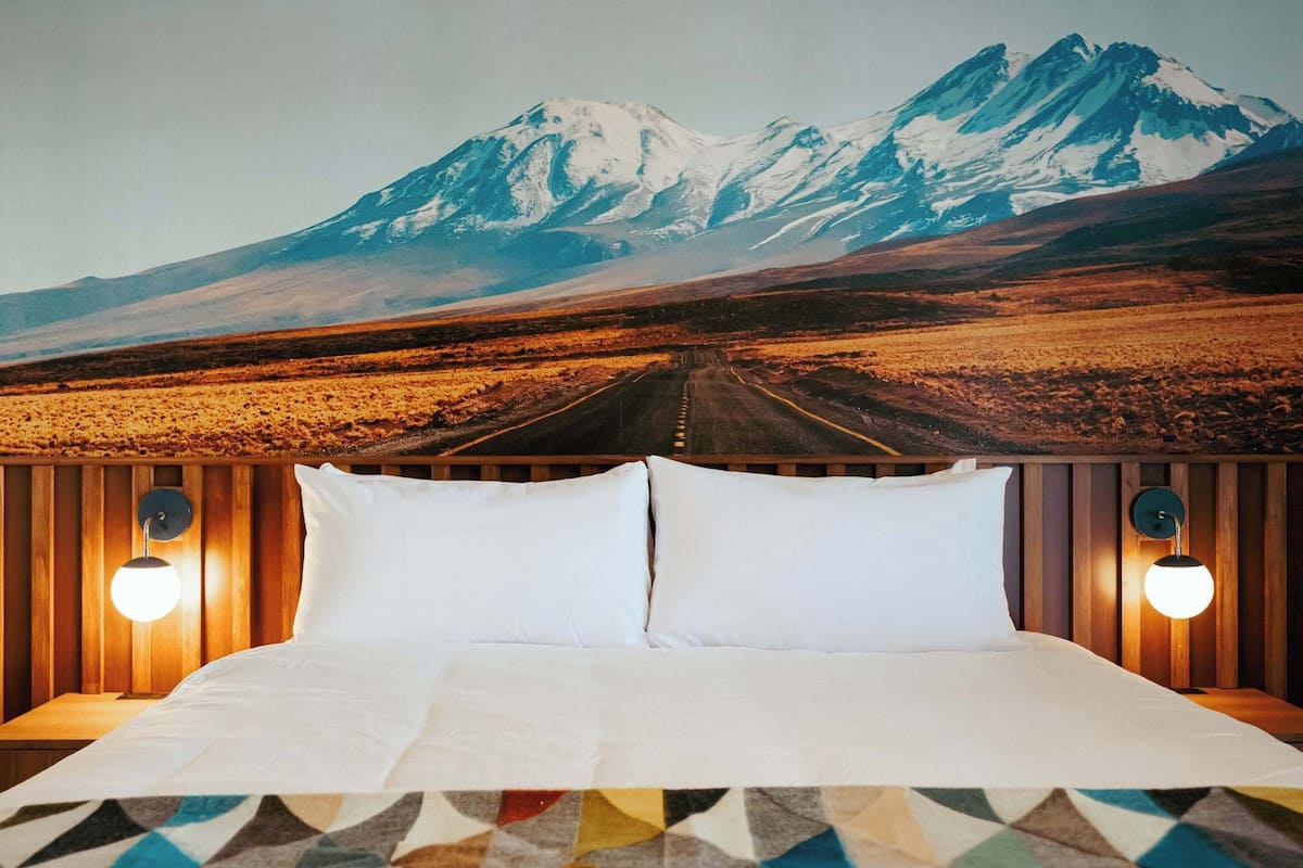Una cama con sábanas blancas, dos almohadas y un plaid estampado con motivos geométricos.