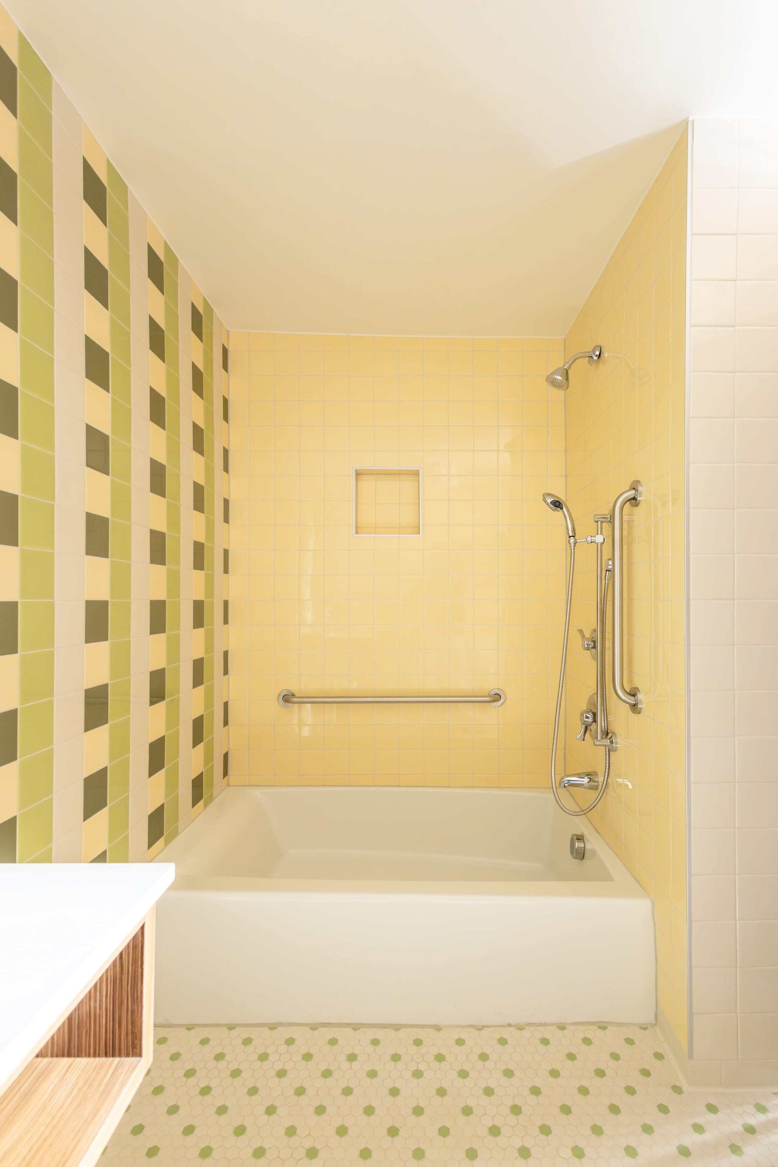Un baño con bañera, barras de apoyo y suelo de baldosas.