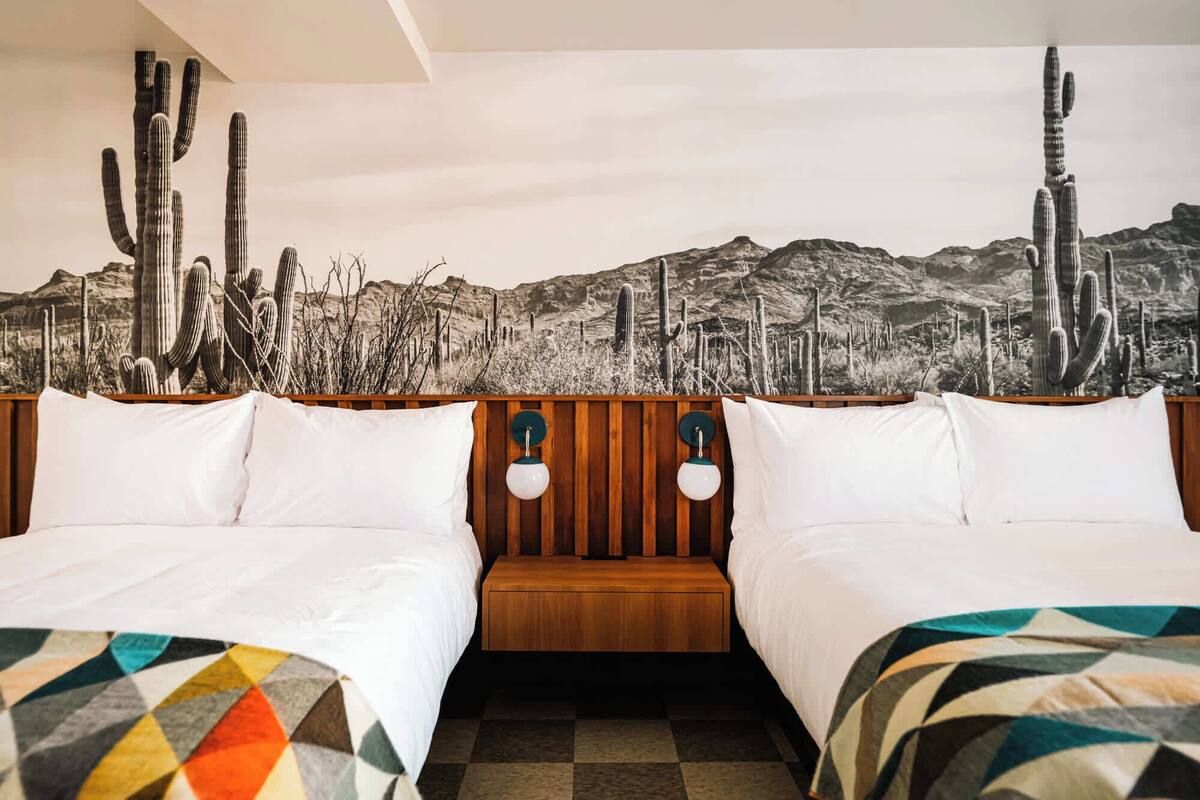 Habitación de hotel con dos camas, cabecero de madera y un mural con temática de desierto en la pared.