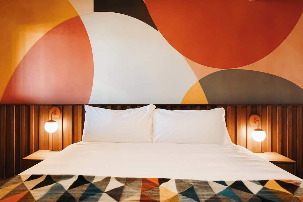 Una habitación de hotel con una cama grande, dos lámparas de noche y un tapete de diseño geométrico.