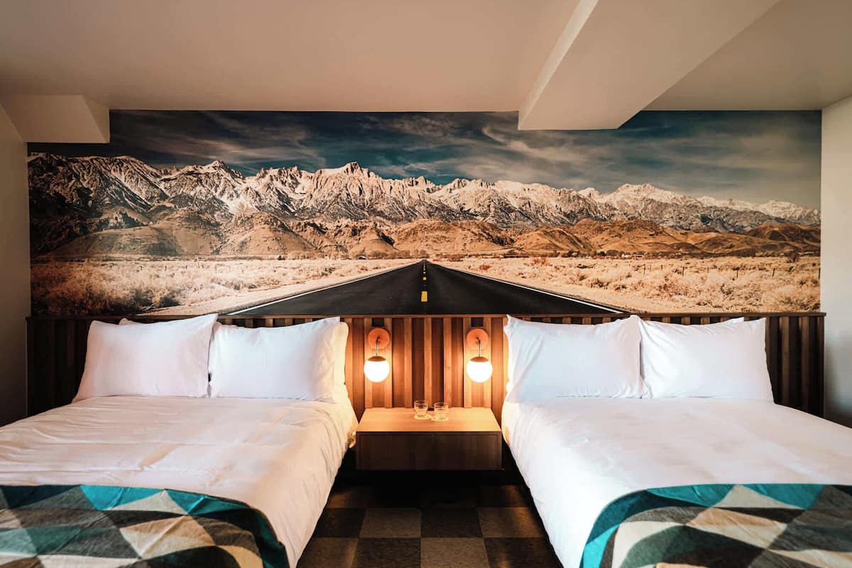 Habitación de hotel con dos camas, un mural con vistas a la montaña y un cabecero de madera con luces.