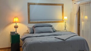 A bedroom with a wooden ceiling, a bed with grey bedding, two bedside lamps, and a window with blinds. - Charming 1-Bedroom In Cozy, Rural Hesperus - Perfect For A Quiet Getaway (Hesperus)