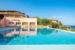 Ein Swimmingpool mit glatter, klarer blauer Wasseroberfläche, umgeben von einem Gebäude mit einer rosafarbenen Fassade und einer Steinmauer.