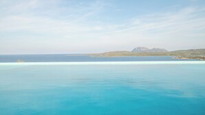 Vista costera con aguas turquesas cristalinas, una montaña distante y una pequeña isla.