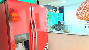 A kitchen with a red refrigerator, teal cabinets, and a decorative orange light fixture. - Complete house 5 bedrooms | Laureles Co-Living (Medellín)