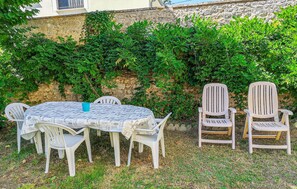 Een terras buiten met een ronde tafel, bedekt met kranten, omringd door witte plastic stoelen.