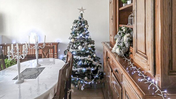A dining area with a Christmas tree, a white table, and a wooden cabinet.