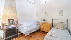 Ein Schlafzimmer mit zwei Einzelbetten, einer Holzkommode, einem Steinkamin und einem Fliesenboden.