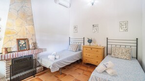 Un dormitorio con dos camas individuales, un aparador de madera, una chimenea de piedra y suelo de baldosas.