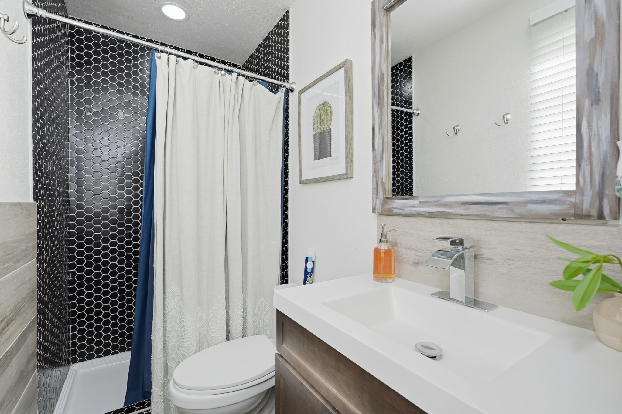 Une salle de bain avec un lavabo blanc, un miroir, un rideau de douche et des toilettes.