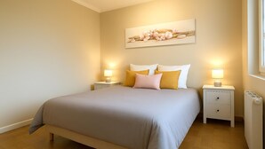 Una camera da letto ordinata con un letto, due comodini, un tavolino, un termosifone e un'opera d'arte appesa al muro.