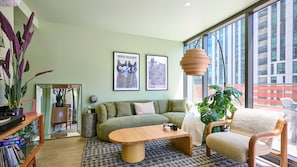 A modern living room with a green sofa, a wooden coffee table, and a large window offering a view of a building. - Sage Zen Muse Docklands Retreat (Docklands)