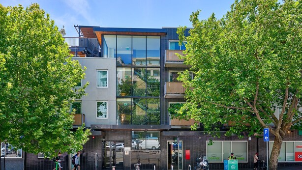 Un edificio moderno de varios pisos con grandes ventanales, balcones y una cafetería en la planta baja.